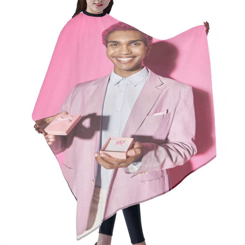 Personality  Handsome Man Smiling At Camera Unnaturally And Showing Small Pink Present On Pink Backdrop Hair Cutting Cape