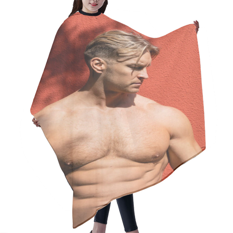 Personality  A Shirtless, Muscular Blonde Man With A Defined Six-pack Poses Against A Red Wall, Looking Down With A Serious Expression. Hair Cutting Cape