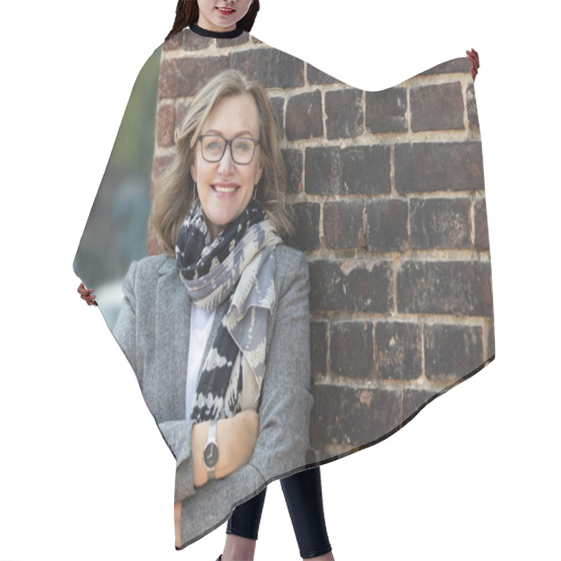 Personality   Portrait Of A Happy Beautiful Woman, 55 Years Old, Smiling. On The Street In The City, On The Background Of The Old Wall Of Red Brick. Hair Cutting Cape