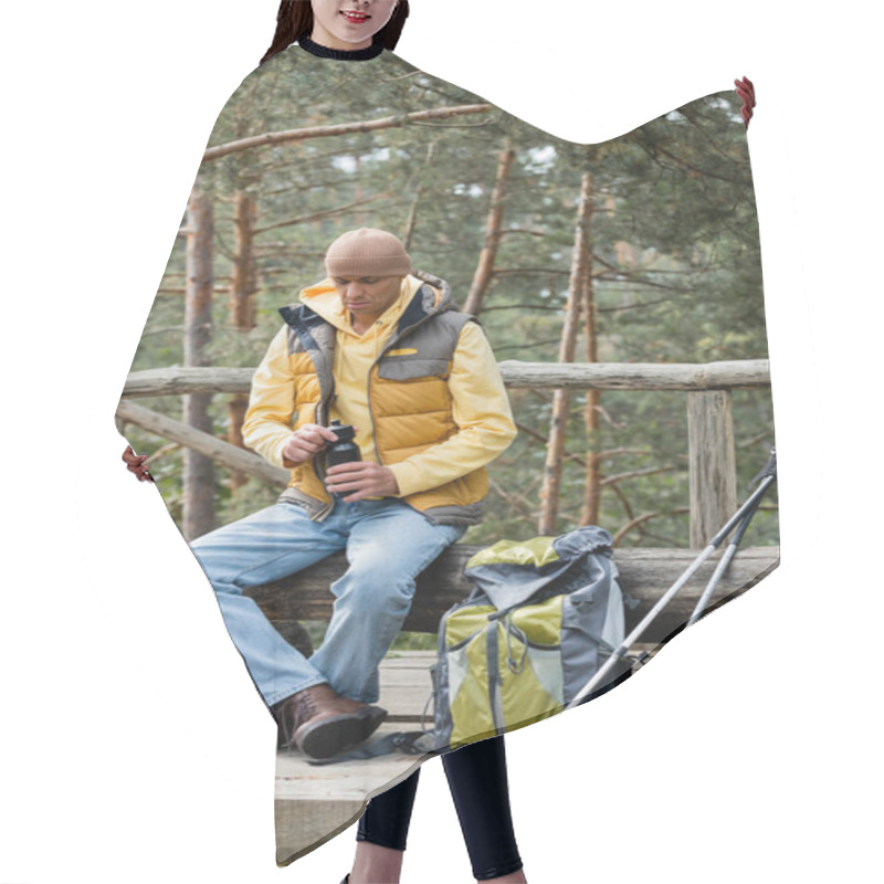 Personality  Tourist In Warm Vest Opening Thermo Bottle During Halt On Log Bench Near Backpack And  Trekking Poles Hair Cutting Cape