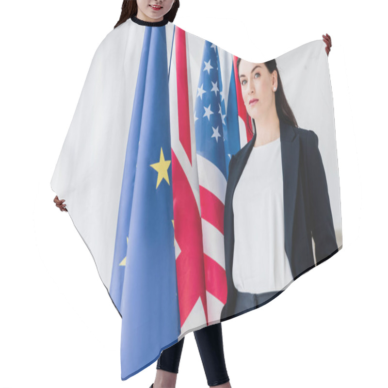 Personality  Beautiful Diplomat Standing With Hands In Pockets Near Flags And Looking At Camera  Hair Cutting Cape