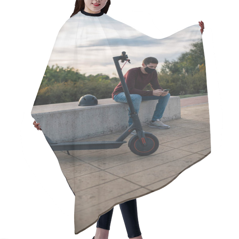 Personality  Young Man On An Electric Skateboard Using A Mobile Phone Sitting On A Bench With His Helmet. Alternative Transport. Hair Cutting Cape