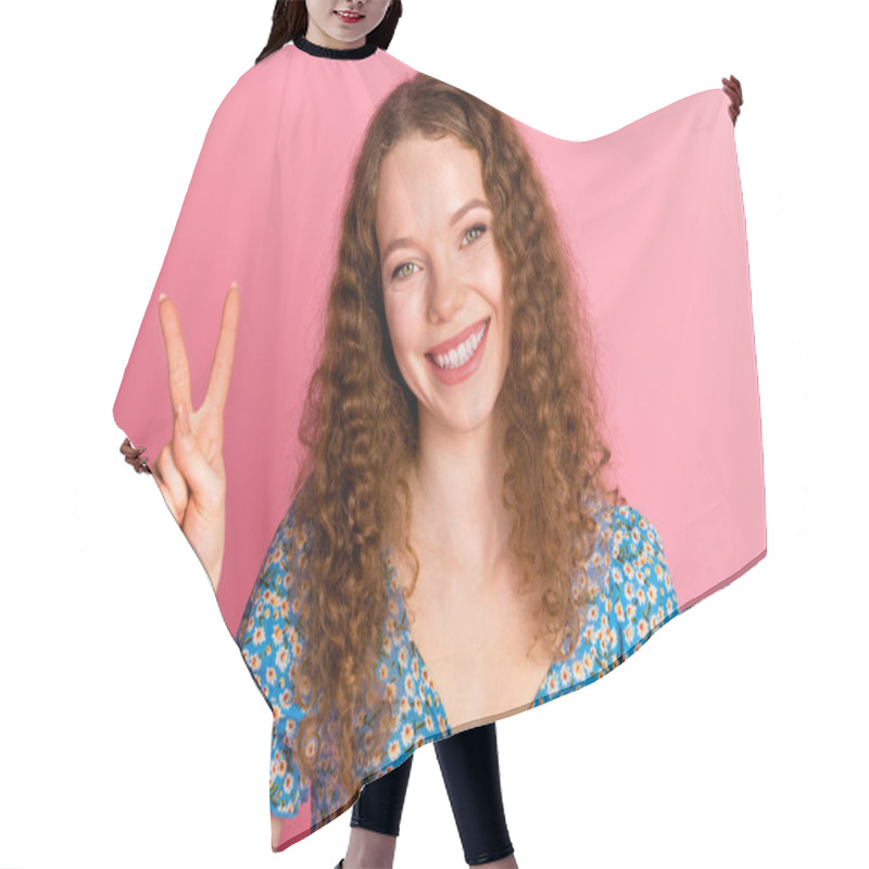 Personality  Joyful Woman With Curly Hair In A Floral Dress Giving A Peace Sign. Bright Smile And Positive Vibes On A Pink Backdrop. Hair Cutting Cape