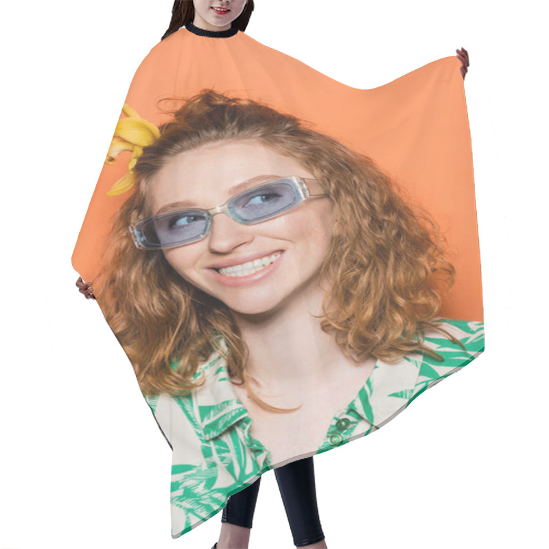 Personality  Portrait Of Joyful Young Redhead Woman With Orchid Flower In Hair And Blue Sunglasses Looking Away And Standing On Orange Background, Summer Casual And Fashion Concept  Hair Cutting Cape