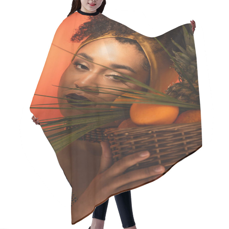 Personality  Young Adult African American Woman Holding Basket With Exotic Fruits Near Face On Orange Hair Cutting Cape