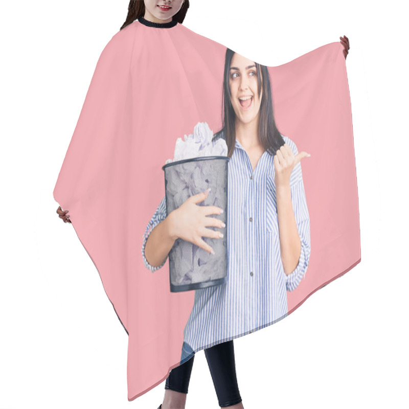 Personality  Young Beautiful Girl Holding Paper Bin Full Of Crumpled Papers Pointing Thumb Up To The Side Smiling Happy With Open Mouth  Hair Cutting Cape