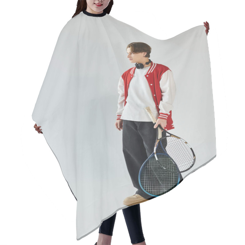 Personality  A Young Man In A Trendy Bomber Jacket Stands Confidently, Holding Tennis Rackets In A Studio. Hair Cutting Cape