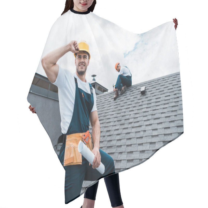 Personality  Selective Focus Of Happy Repairman Holding Rolled Paper While Coworker Repairing Roof  Hair Cutting Cape