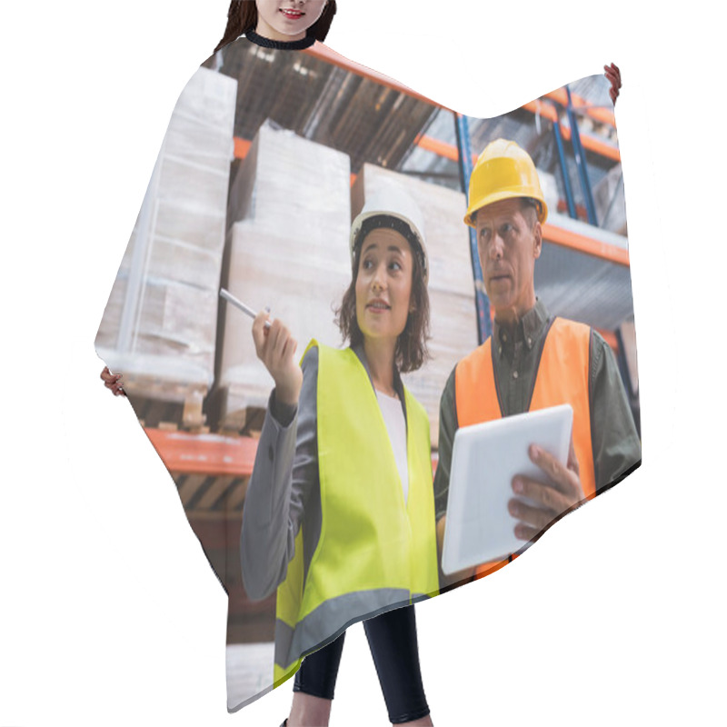 Personality  Supervisor In Hard Hat Holding Tablet While Discussing Work To Happy Female Employee In Warehouse Hair Cutting Cape