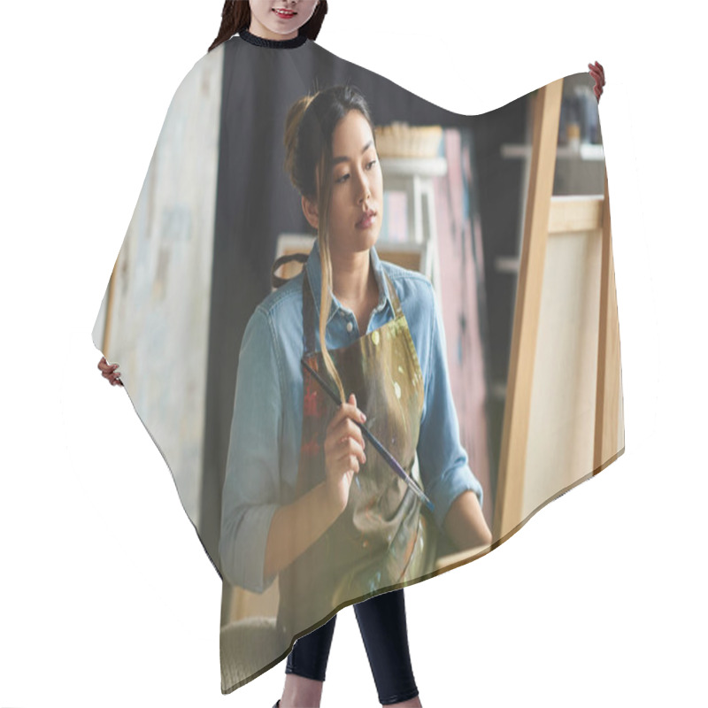 Personality  An Asian Artist In An Apron Stands In Her Studio, Thoughtfully Considering Her Next Brushstroke On A Canvas. Hair Cutting Cape