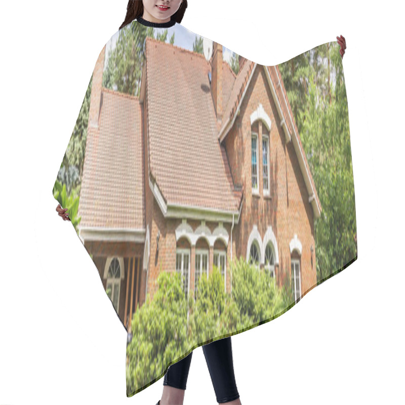 Personality  A Red Brick English Style Classic House With A Steep Roof And Large Windows Surrounded By Trees And Green Plants. Panorama. Hair Cutting Cape