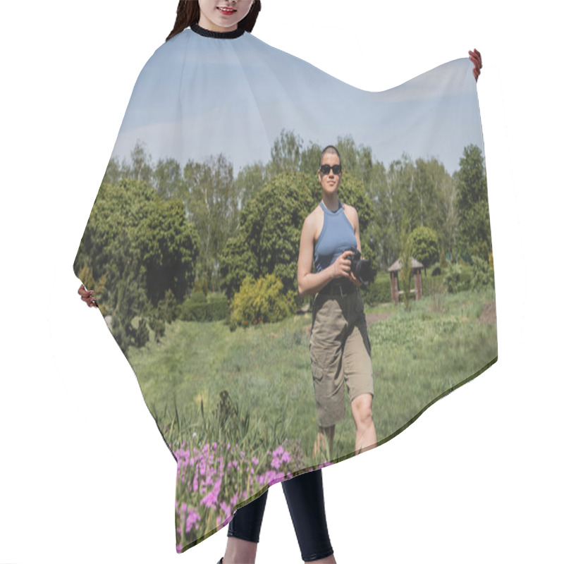 Personality  Young Short Haired Woman Tourist In Sunglasses Holding Digital Camera While Standing Near Blurred Flowers With Blurred Scenic Landscape At Background, Translation Of Tattoo: Love Hair Cutting Cape