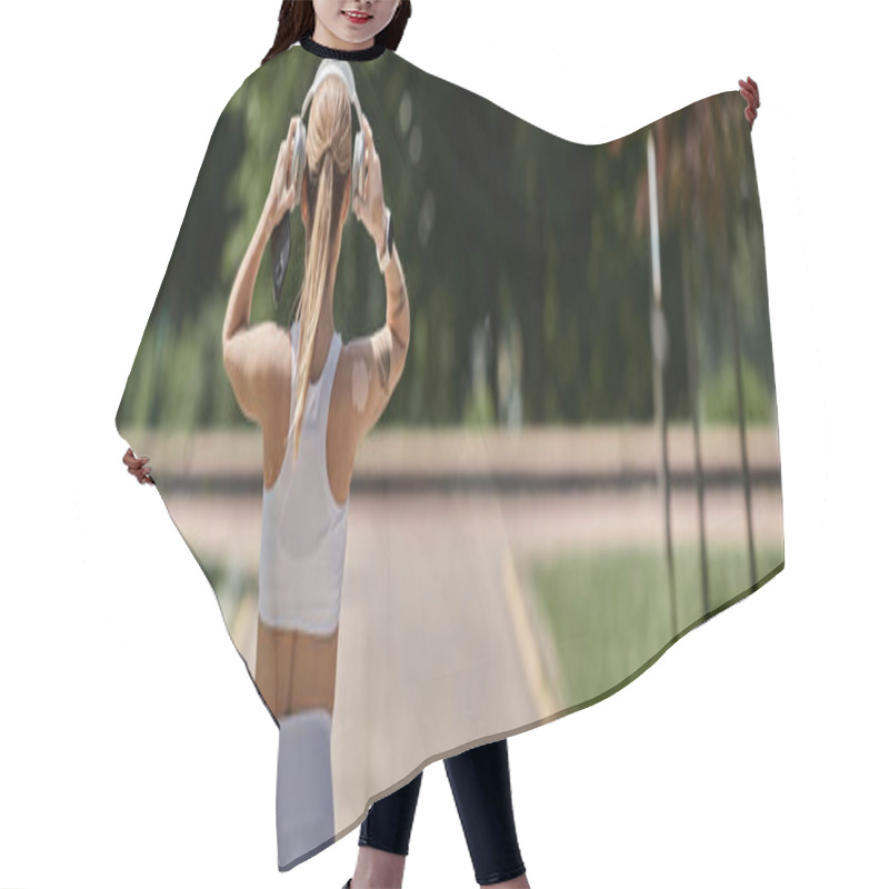 Personality  A Young Woman In Athletic Wear Adjusts Her Headphones As She Walks Through A Park. Hair Cutting Cape