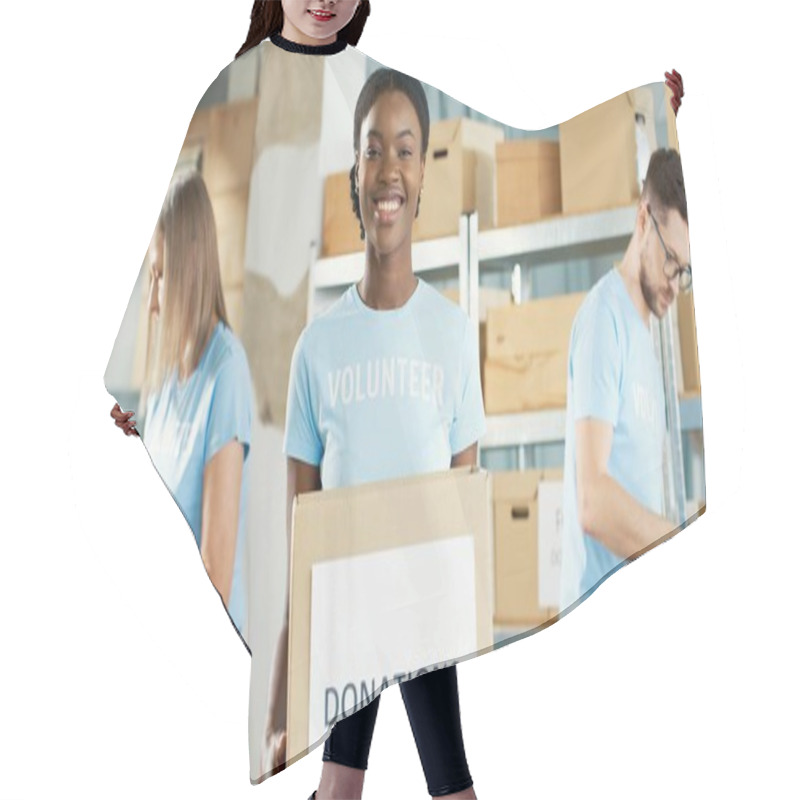 Personality  Close Up Portrait Of African American Young Happy Female Volunteer Holding In Hands Donations Box, Looking At Camera And Smiling. Charity Organization. Colleagues Packing Donations On Background Hair Cutting Cape