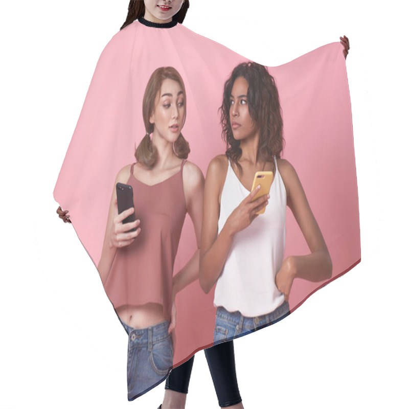 Personality  Young Two Women Using Mobile Phone While Brunette Woman Looks At Smartphone Her Friend On Pink Background. Secret Privacy In Social Media. Hair Cutting Cape