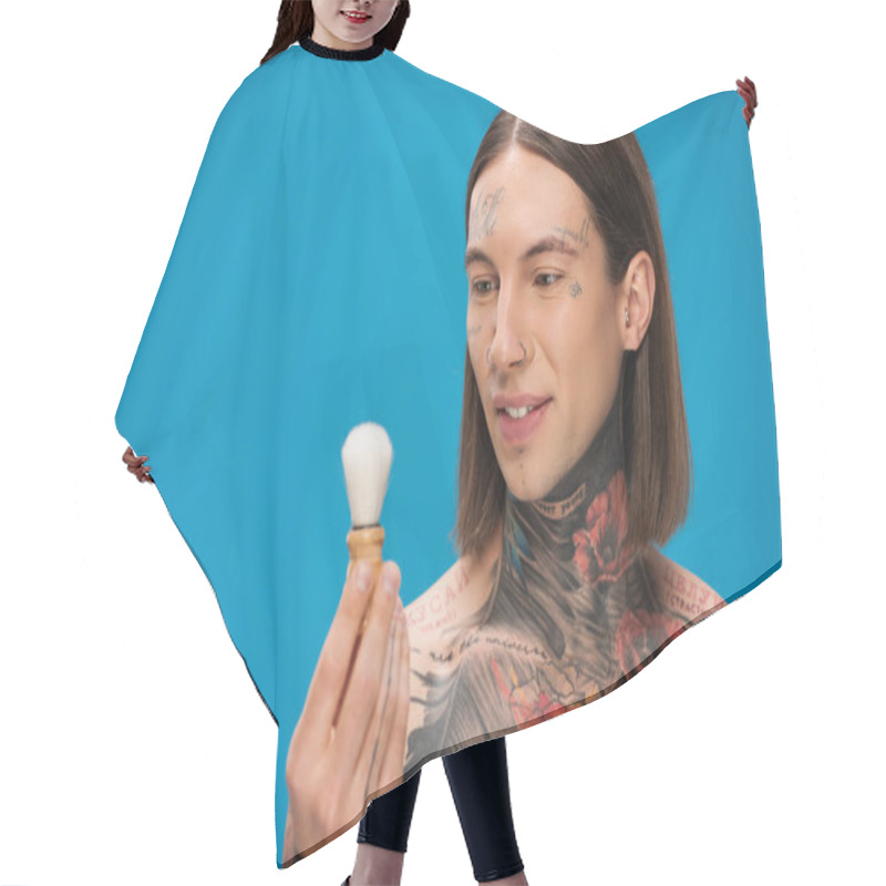 Personality  Cheerful And Tattooed Man Looking At Shaving Brush Near Face Isolated On Blue Hair Cutting Cape