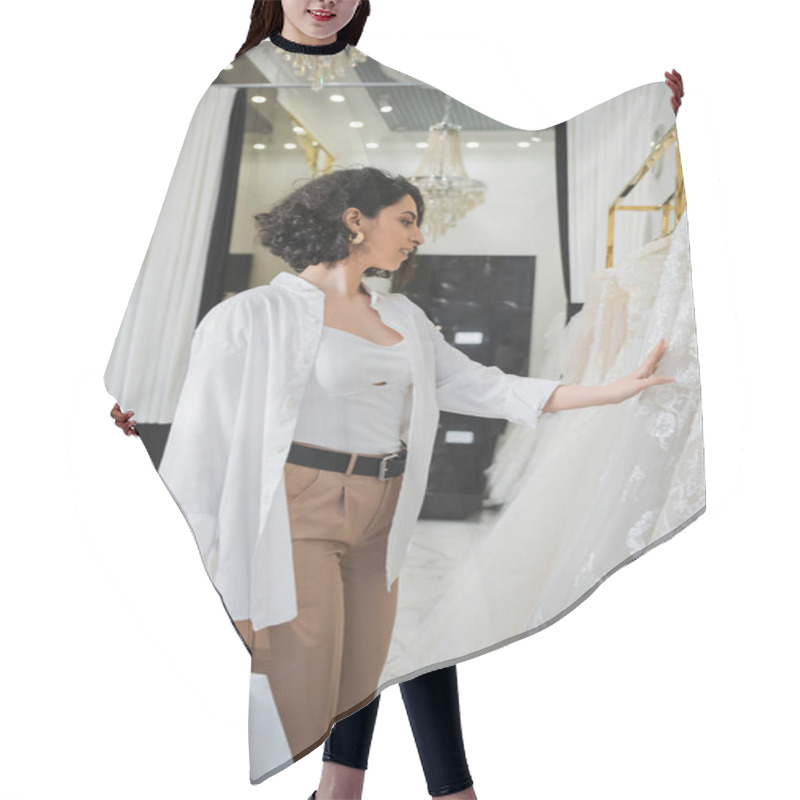 Personality  Side View Of Stylish And Happy Middle Eastern Woman With Brunette And Wavy Hair Standing In Beige Pants With White Shirt And Holding Shopping Bags While Choosing Wedding Dress In Bridal Salon  Hair Cutting Cape