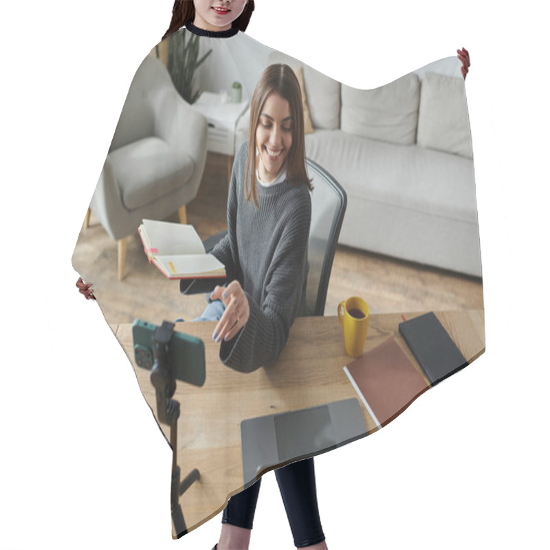 Personality  A Young Woman Smiles While Filming A Video At Her Home Office Desk. Hair Cutting Cape