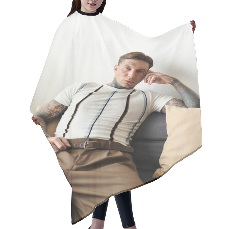 Personality  A Tattooed Young Man Relaxes Confidently On A Couch In A Modern Living Space. Hair Cutting Cape