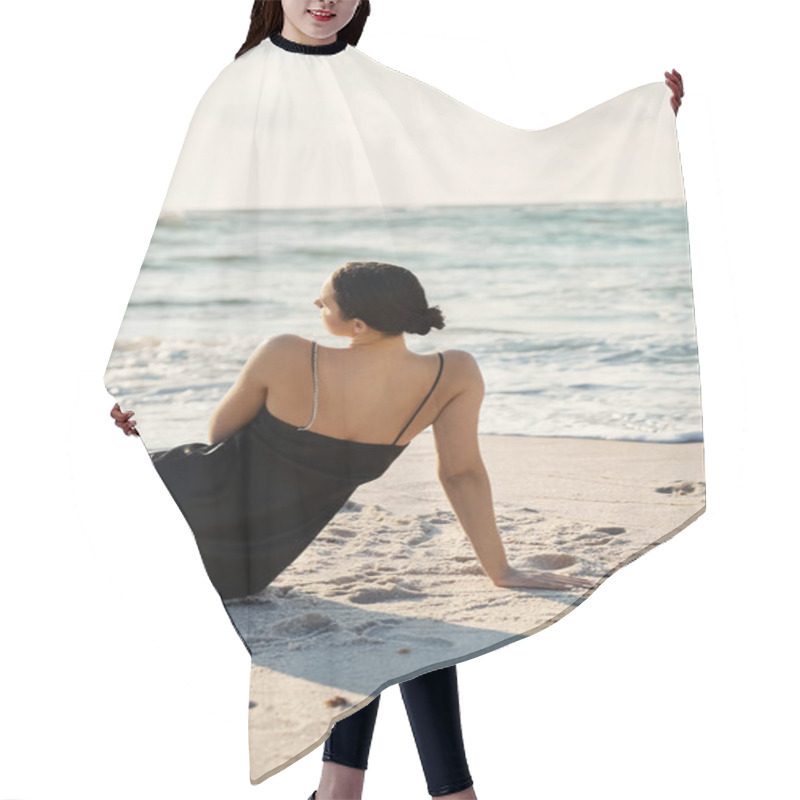 Personality  A Young Woman In A Black Sundress Sits On The Sand, Facing The Ocean Waves, On Miami Beach, Florida. Hair Cutting Cape