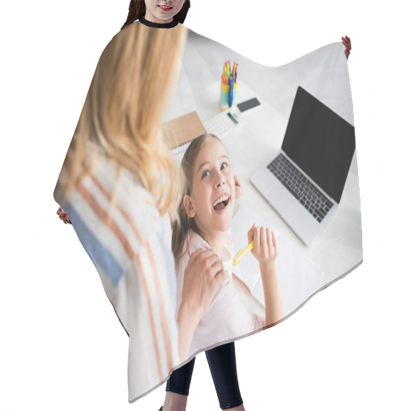 Personality  Selective Focus Of Positive Kid Looking At Mother While Holding Pen Near Notebook And Laptop On Table  Hair Cutting Cape