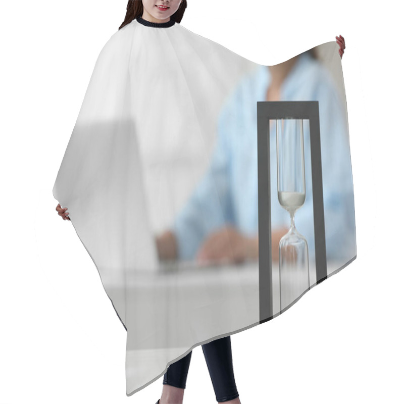 Personality  Hourglass With Flowing Sand On White Table. Woman Using Laptop Indoors, Selective Focus Hair Cutting Cape