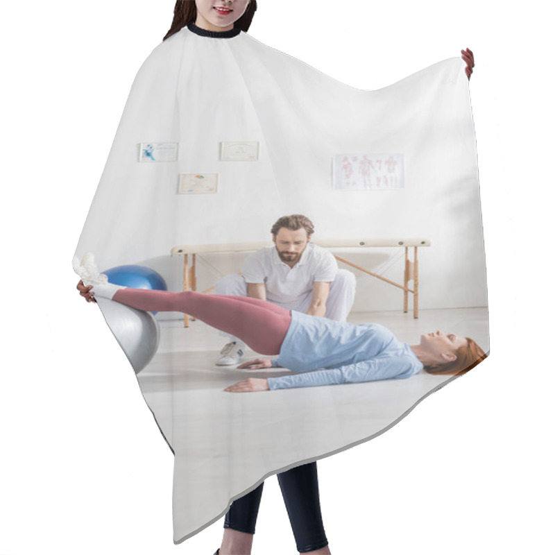 Personality  Bearded Physiotherapist Near Woman Lying On Floor And Working Out With Fitness Ball In Rehab Center Hair Cutting Cape