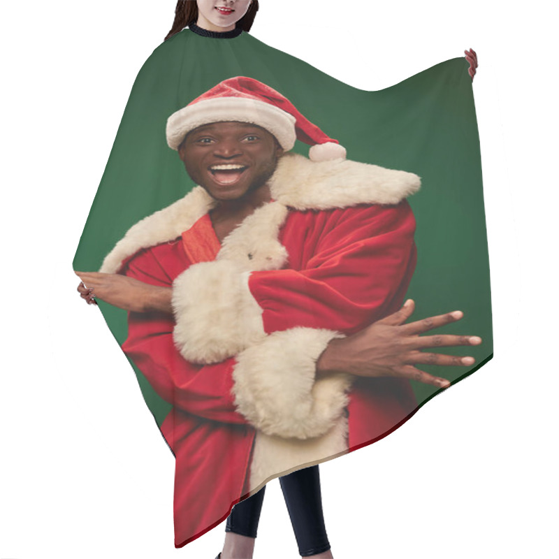 Personality  Overjoyed African American Man In Santa Claus Costume Gesturing And Looking At Camera On Green Hair Cutting Cape