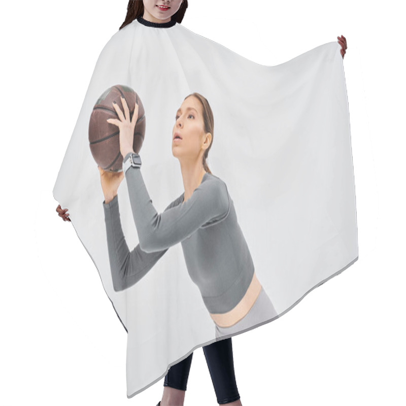 Personality  A Sporty Young Woman Gracefully Holds A Basketball In Her Right Hand Against A Neutral Grey Background. Hair Cutting Cape