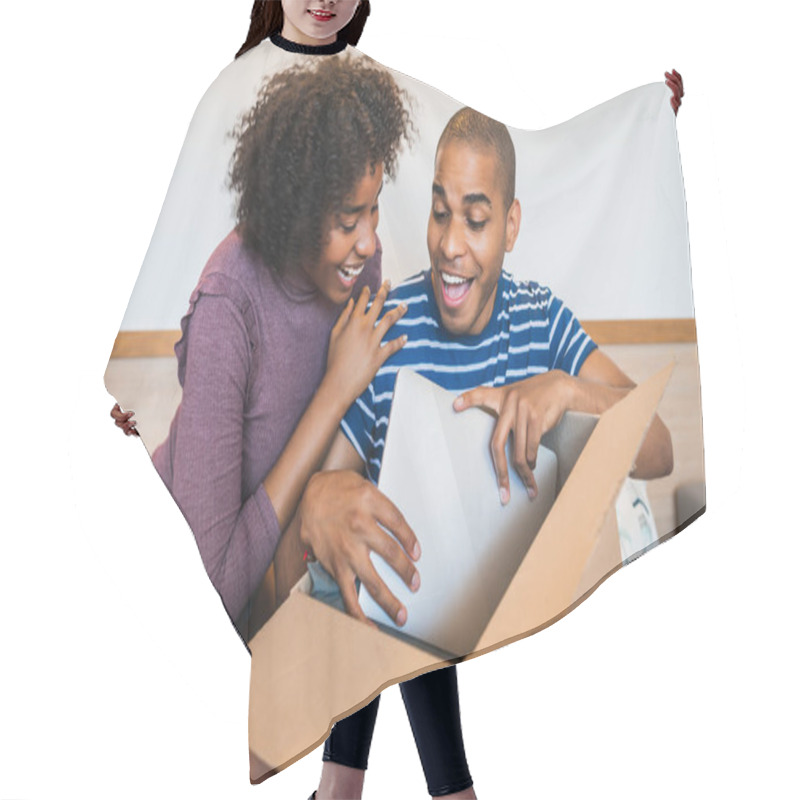 Personality  Portrait Of Happy Young Latin Couple Opening A Package With A Laptop Inside, At Home. Delivery, Shipping And Postal Service Concept. Hair Cutting Cape