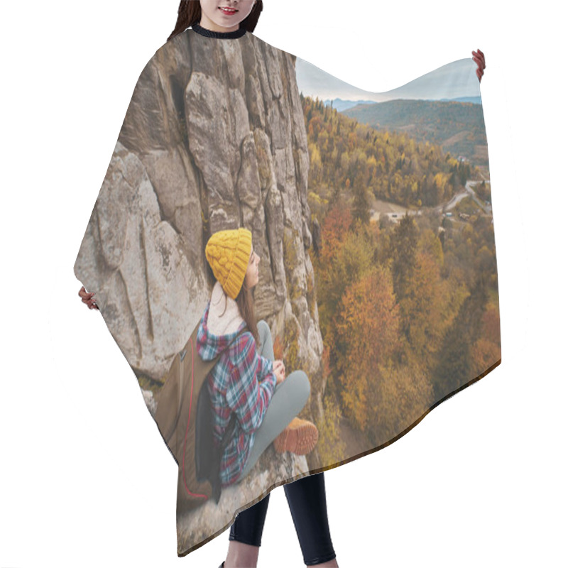 Personality  Woman Tourist In Yellow Hat With Backpack Sitting On Cliff Edge With Autumn Forest And Valley View. Adventure Vacations Tour Outdoor To National Park In Ukraine, Tustan. Hair Cutting Cape