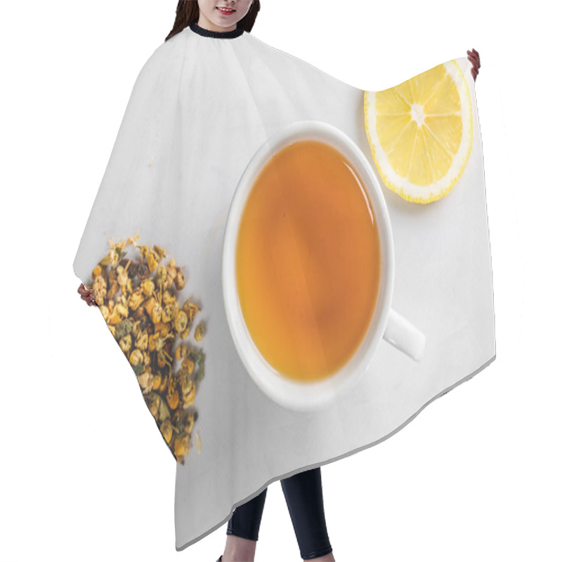 Personality  A Cup Of Green Tea With Dried Chamomile Flowers And A Slice Of Cut Lemon On A White Background. Diet And Healthy Drink. Flatley. Top View Hair Cutting Cape