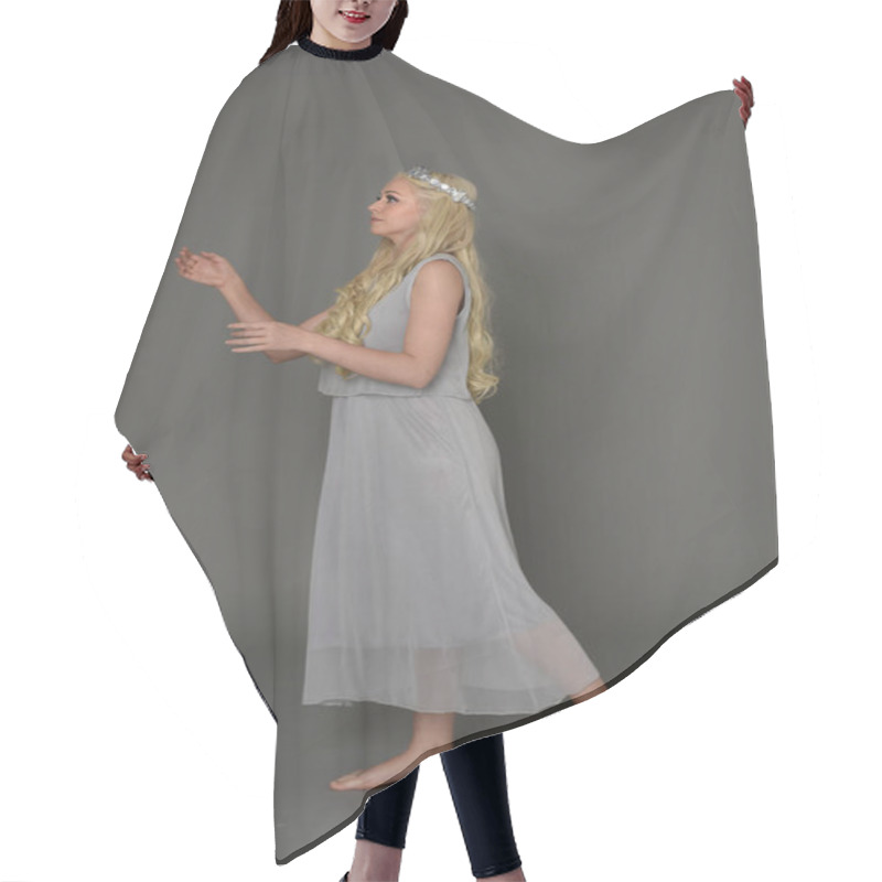 Personality  Full Length Portrait Of Blonde Girl Wearing Crow And Grey Dress, Standing Pose In Side Profile.  Grey Studio Background. Hair Cutting Cape