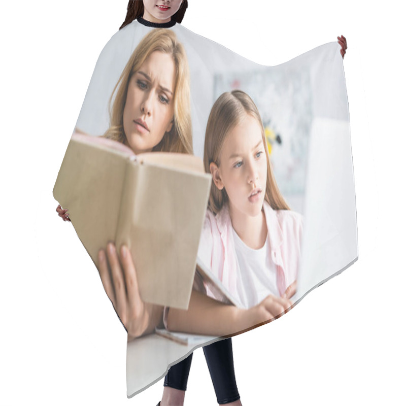 Personality  Selective Focus Of Concentrated Woman Reading Book Near Daughter Using Laptop At Table  Hair Cutting Cape