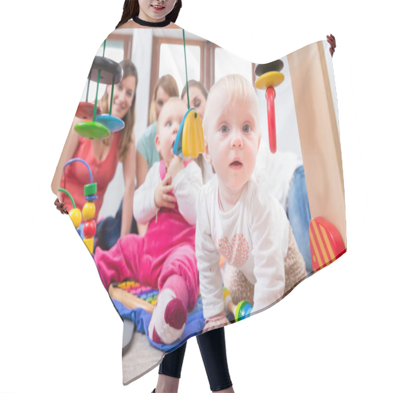 Personality  Cute Baby Girl Showing Progress And Curiosity By Trying To Reach Multicolored Wooden Toys, While Sitting On The Floor With Her Mother And A Family Friend Hair Cutting Cape