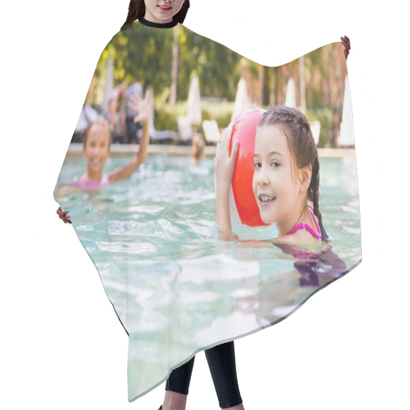 Personality  Selective Focus Of Girl Looking At Camera While Holding Inflatable Ball Near Friend Waving Hand In Swimming Pool Hair Cutting Cape