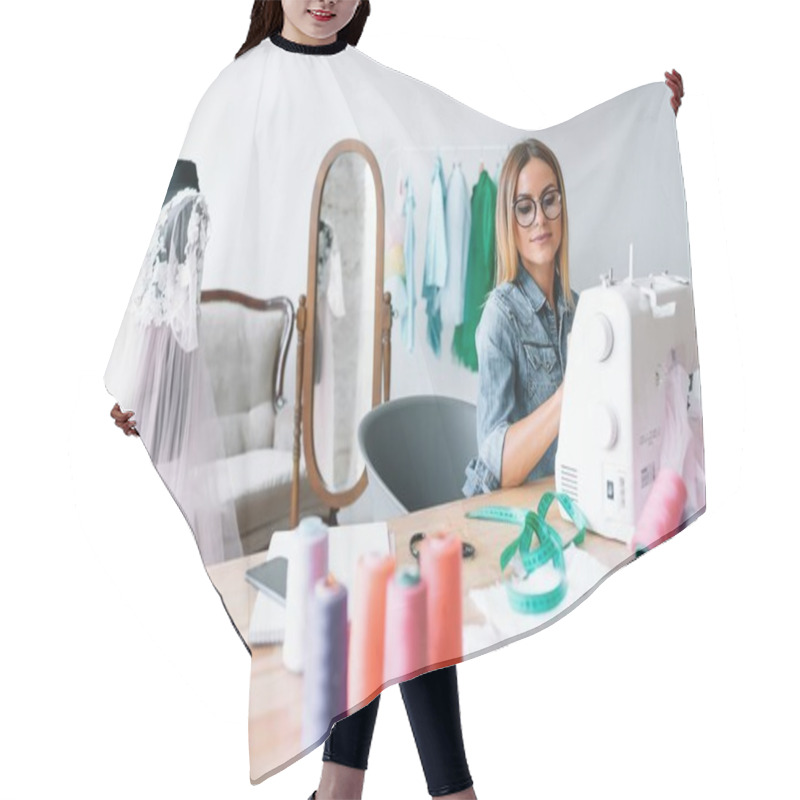 Personality  Smiling Fashion Designer Looking At Camera At Workplace, Dressmaker, Needlewoman Or Tailor Shop Owner Sitting At Desk With Color Swatches Pantone And Embroidery Design Sketches On The Wall, Portrait Hair Cutting Cape