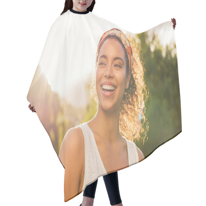 Personality  Portrait Of Beautiful African American Woman Smiling And Looking Away At Park During Sunset. Outdoor Portrait Of A Smiling Black Girl. Happy Cheerful Girl Laughing At Park With Colored Hair Band. Hair Cutting Cape