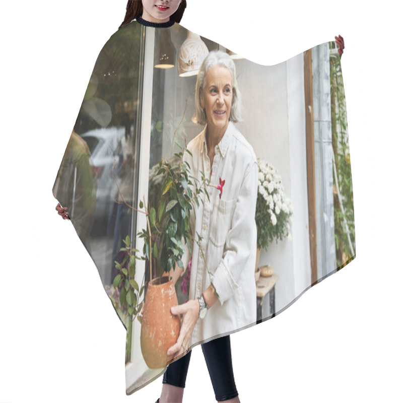 Personality  A Joyful Woman With Silver Hair Carries A Potted Plant, Smiling In A Garden Shops Outdoor Space. Hair Cutting Cape