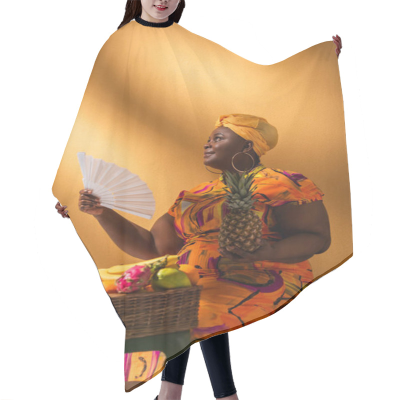 Personality  Middle Aged African American Woman Sitting Near Fruits And Holding Pineapple And Fan On Orange Hair Cutting Cape