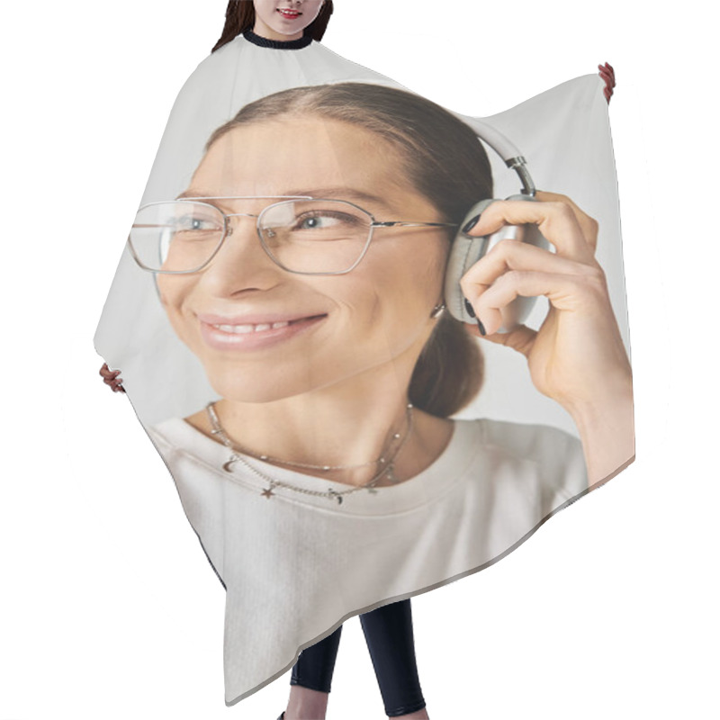 Personality  A Young Woman In A White T-shirt And Glasses Holding A Headset On A Grey Background. Hair Cutting Cape