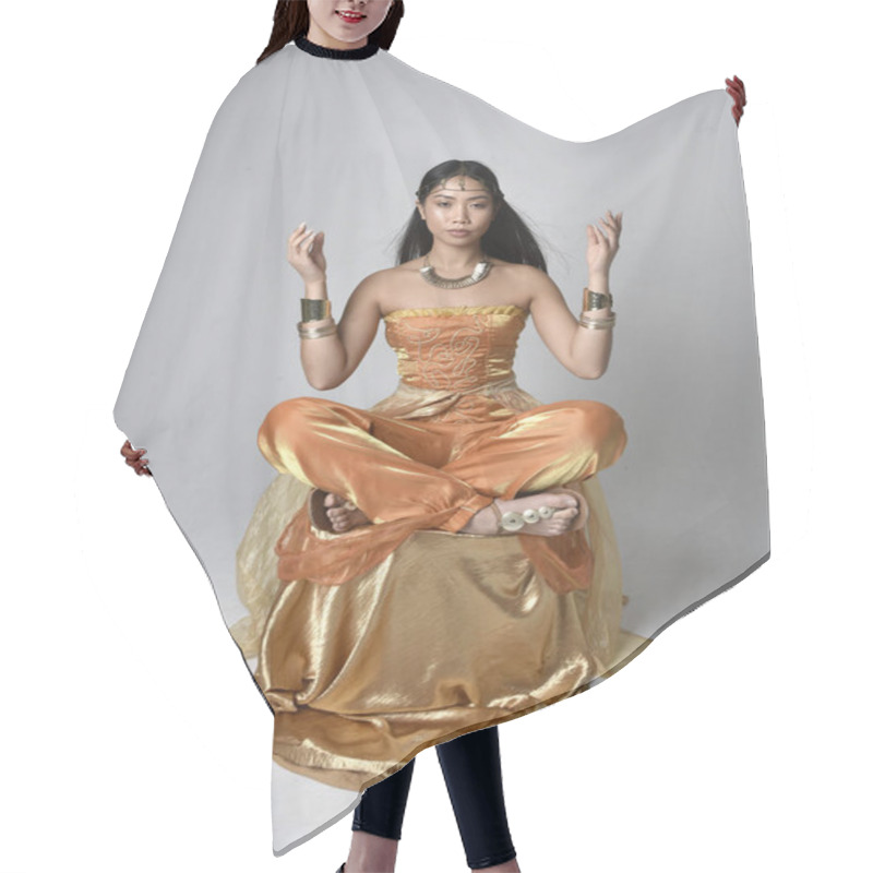 Personality  Full Length Portrait Of Pretty Young Asian Woman Wearing Golden Arabian Robes Like A Genie, Seated Pose, Isolated On Studio Background. Hair Cutting Cape