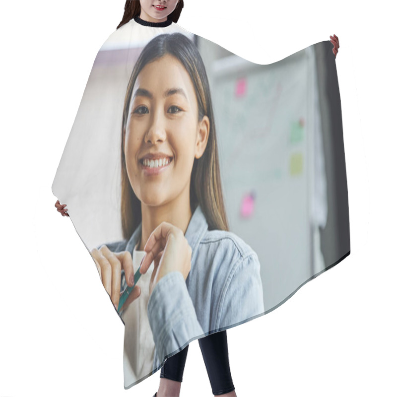 Personality  Portrait Of Young And Charming Asian Businesswoman With Brunette Hair And Cheerful Smile Holding Pen And Looking At Camera In Modern Office, Professional Headshot  Hair Cutting Cape