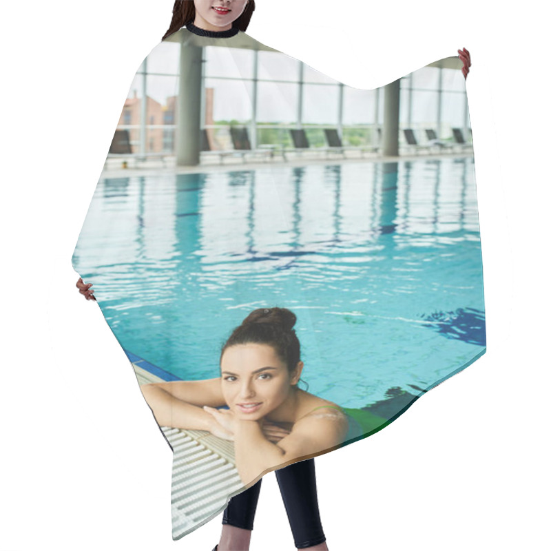 Personality  A Young, Beautiful Brunette Woman In A Swimsuit Relaxing On The Side Of An Indoor Swimming Pool. Hair Cutting Cape