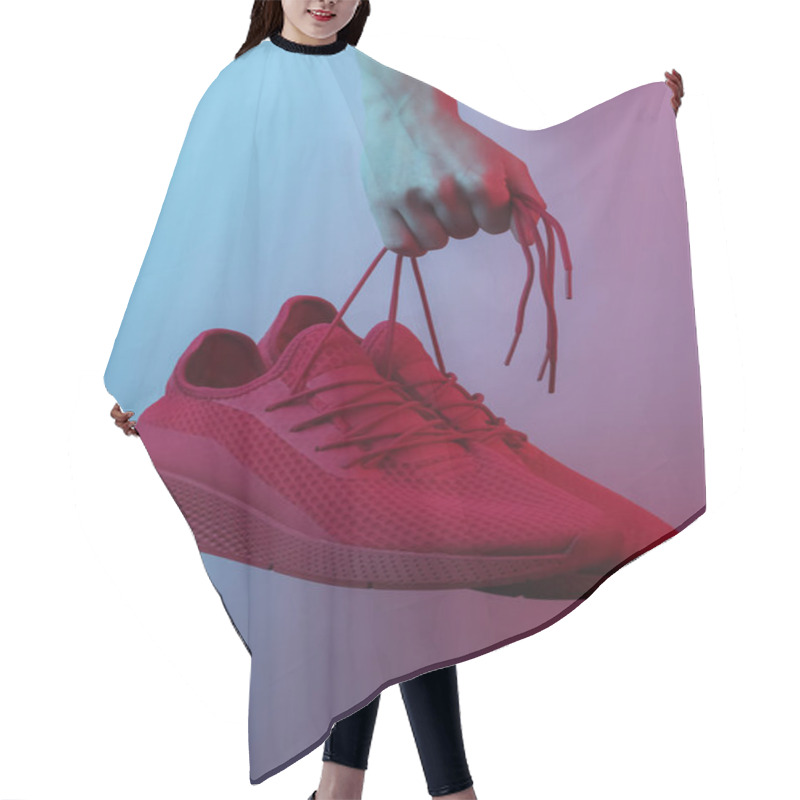 Personality  Female Hand Holds Red Sports Sneakers By The Laces. Creative Pop Art Pink Blue Neon Color. Trendy Gradient Illumination. Night Light Hair Cutting Cape