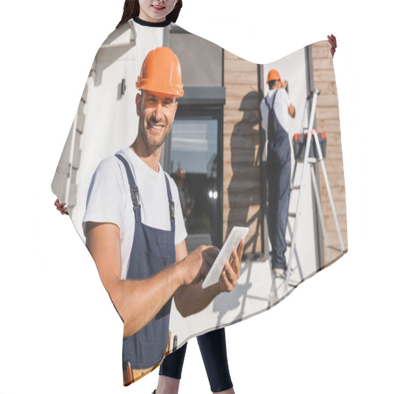 Personality  Selective Focus Of Builder With Digital Tablet Looking At Camera While Colleague Working On Ladder Near House At Background  Hair Cutting Cape