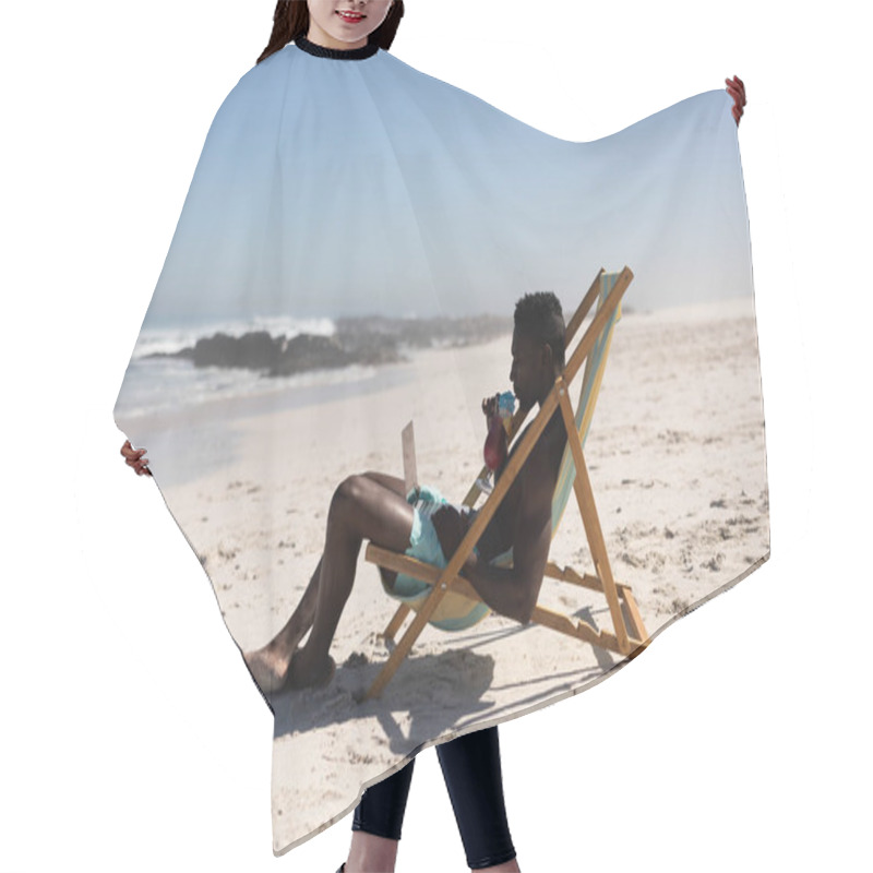 Personality  African American Man Enjoying Free Time On Beach On A Sunny Day, Drinking, Sitting In A Deck Chair, Using His Laptop. Hair Cutting Cape