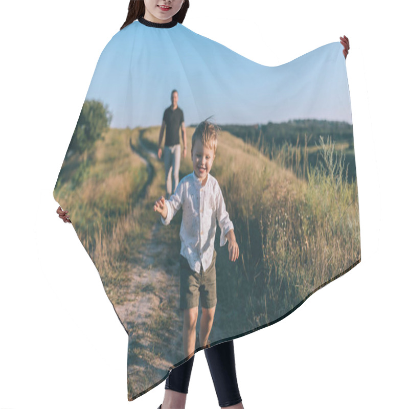 Personality  Adorable Happy Little Boy Running On Rural Path While Father Walking Behind Hair Cutting Cape