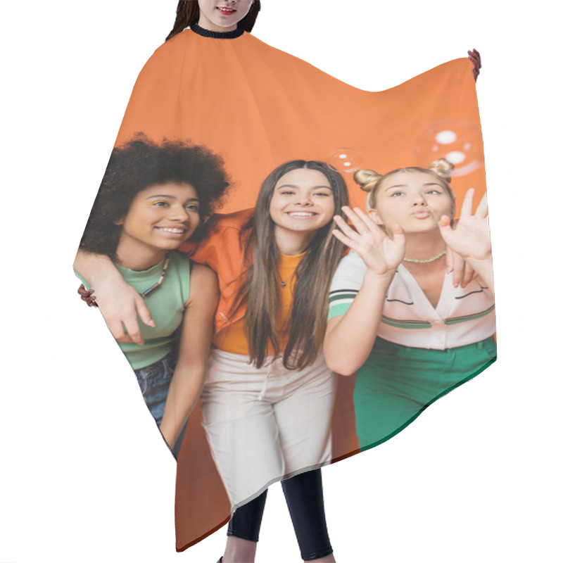 Personality  Cheerful Brunette Teenager Hugging Stylish Multiethnic Girlfriends And Standing Near Soap Bubbles On Orange Background, Multiethnic Teen Fashionistas With Impeccable Style Concept Hair Cutting Cape