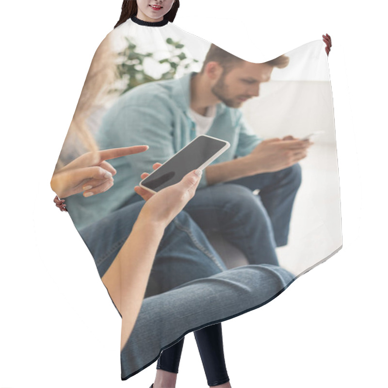 Personality  Selective focus of woman pointing with finger at smartphone with blank screen near boyfriend on couch  hair cutting cape